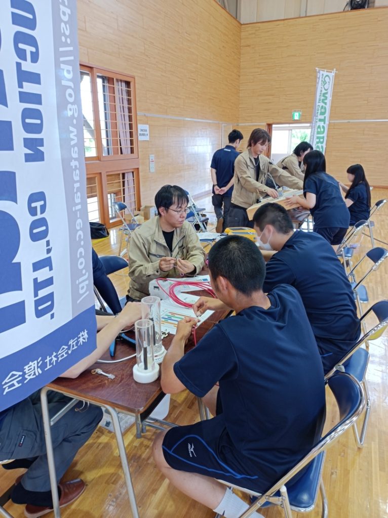 机を挟んで生徒4人と従業員4人が作業をしている